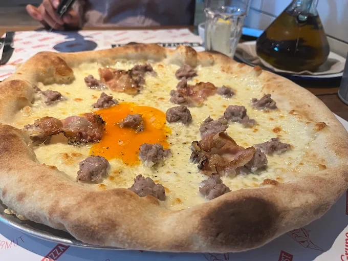 Pizza de Porco Dio con yema de huevo y embutido sobre una mesa del restaurante